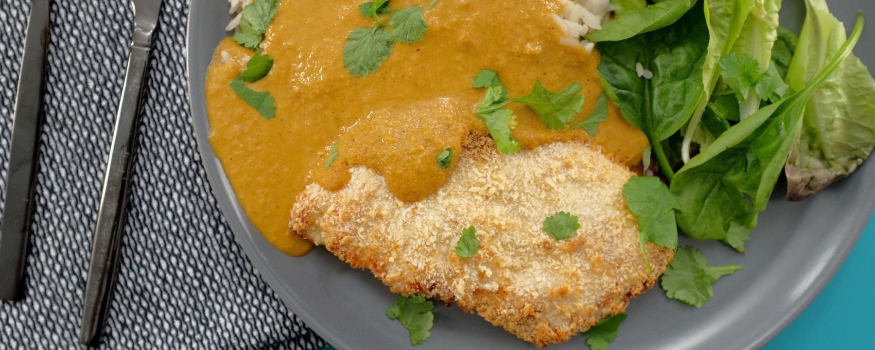 Breaded chicken with curry sauce, white rice and salad leaves on grey plate