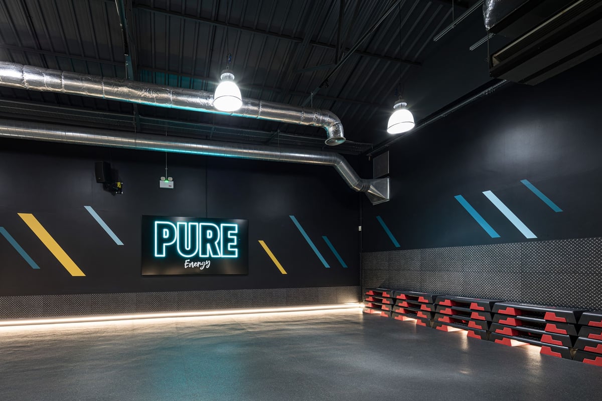 PureGym Dudley Tipton: Black studio interior with neon lights, weight racks, and padded benches.