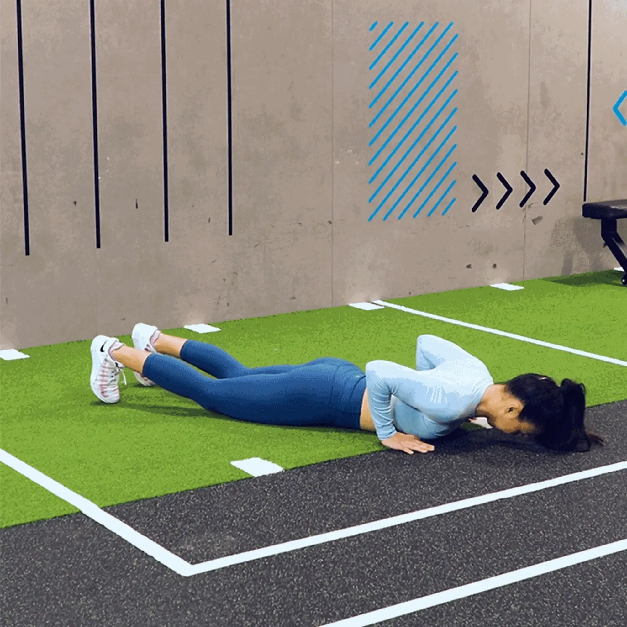 Woman doing push-up exercise on green and black gym floor near wall markings
