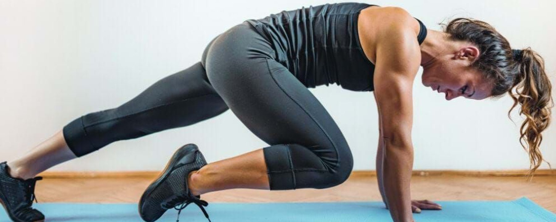 Woman in black sportswear doing mountain climber exercise on blue yoga mat indoors