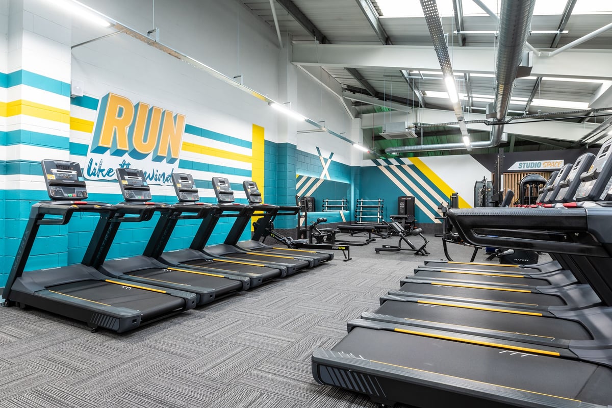 PureGym Guiseley: Rows of treadmills with colourful wall graphics promoting running in a gym setting.