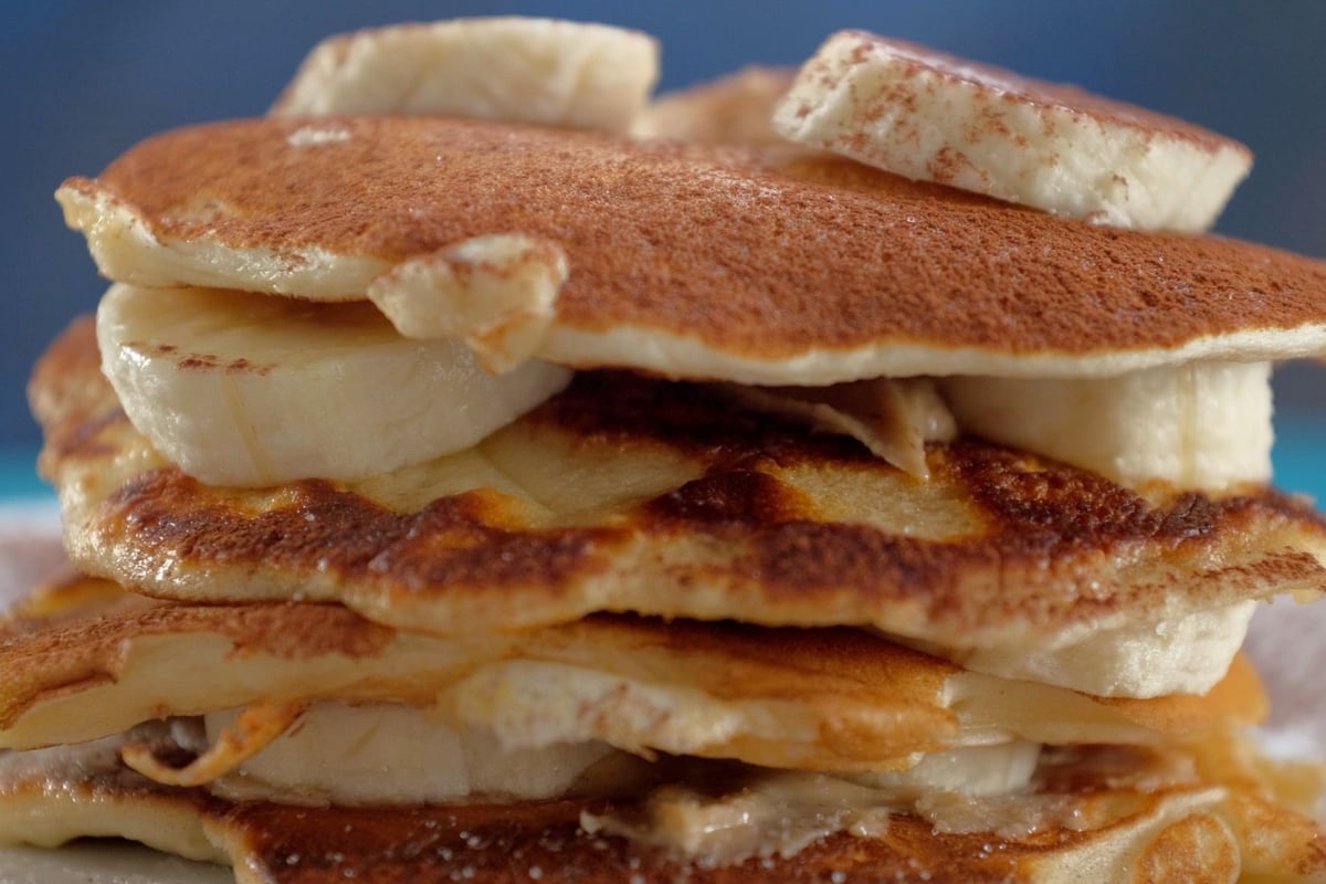 Stack of golden pancakes layered with sliced banana and peanut butter