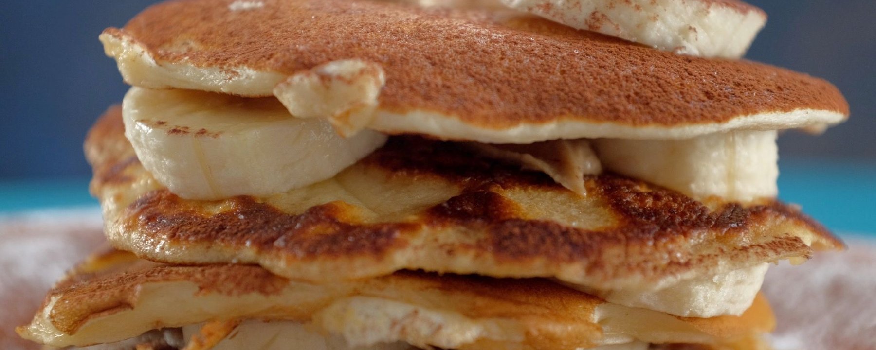 Stack of golden pancakes layered with sliced banana and peanut butter
