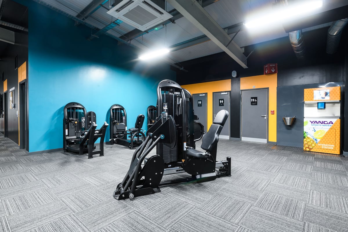 PureGym Swindon Mannington Retail Park: Weight machines, resistance equipment on rubberized flooring with blue accent wall.