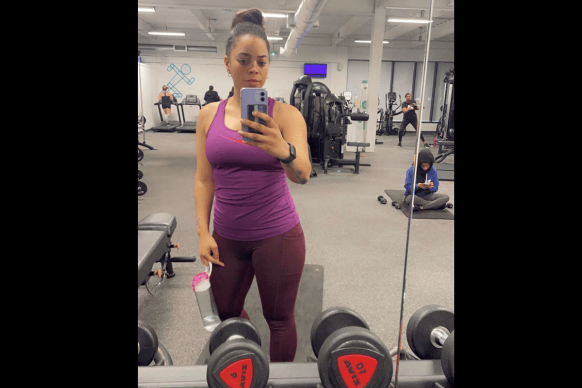 Woman in purple workout clothes taking a mirror selfie in a gym with dumbbells in front