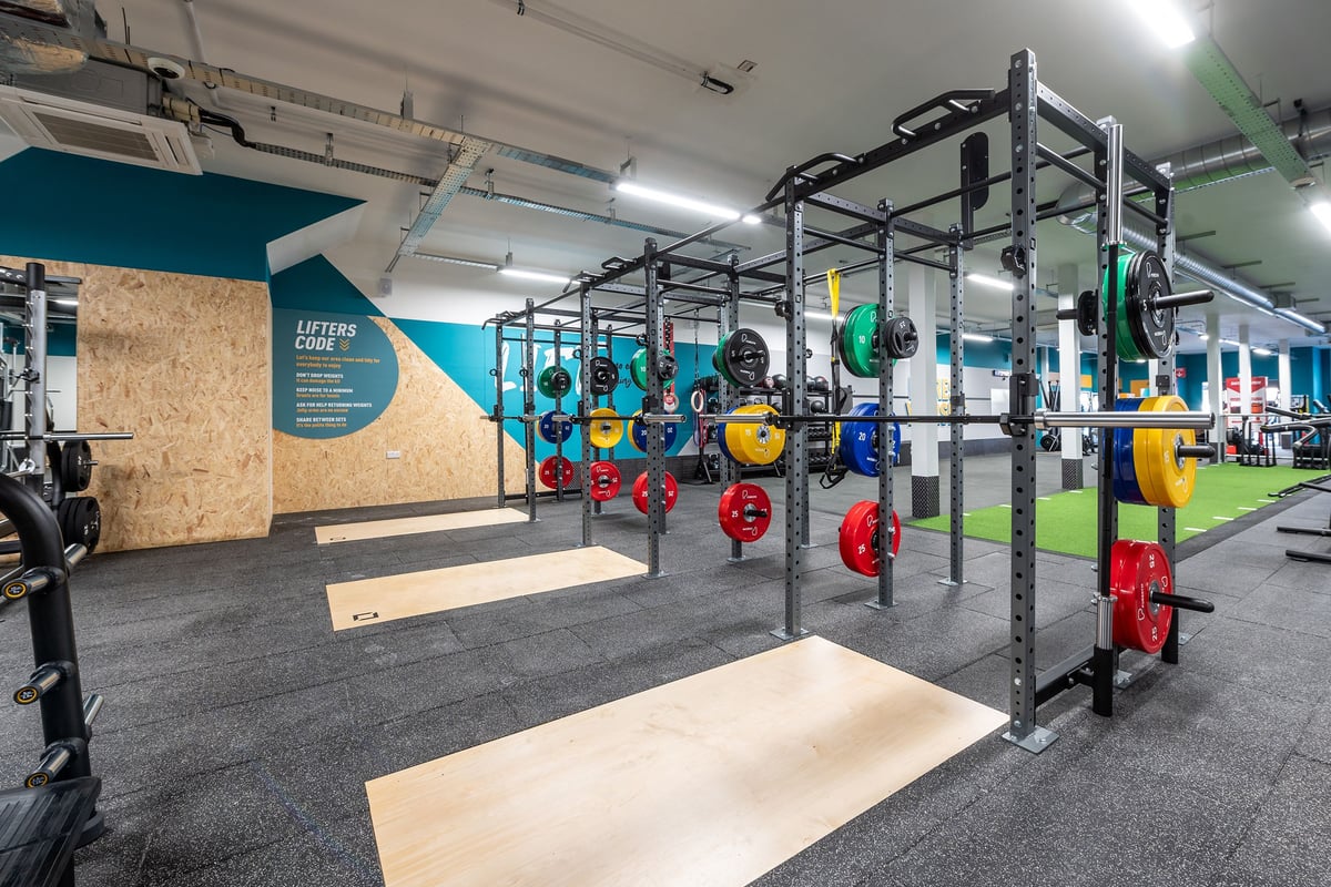 PureGym Guiseley: Power racks, colourful weight plates, rubberised flooring, and motivational branding on walls.