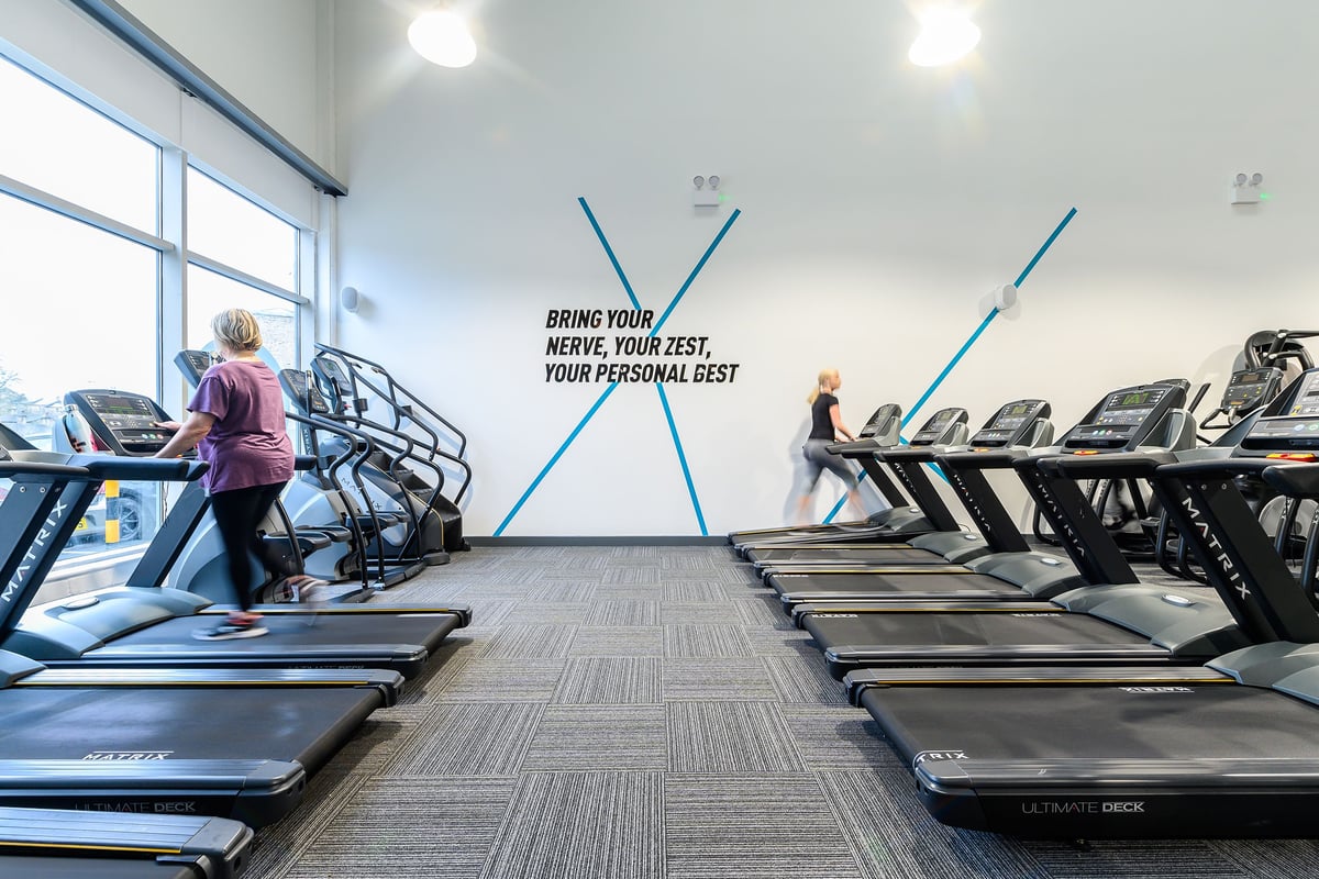 PureGym Glossop: Rows of treadmills in a bright fitness studio with motivational signage on the wall.