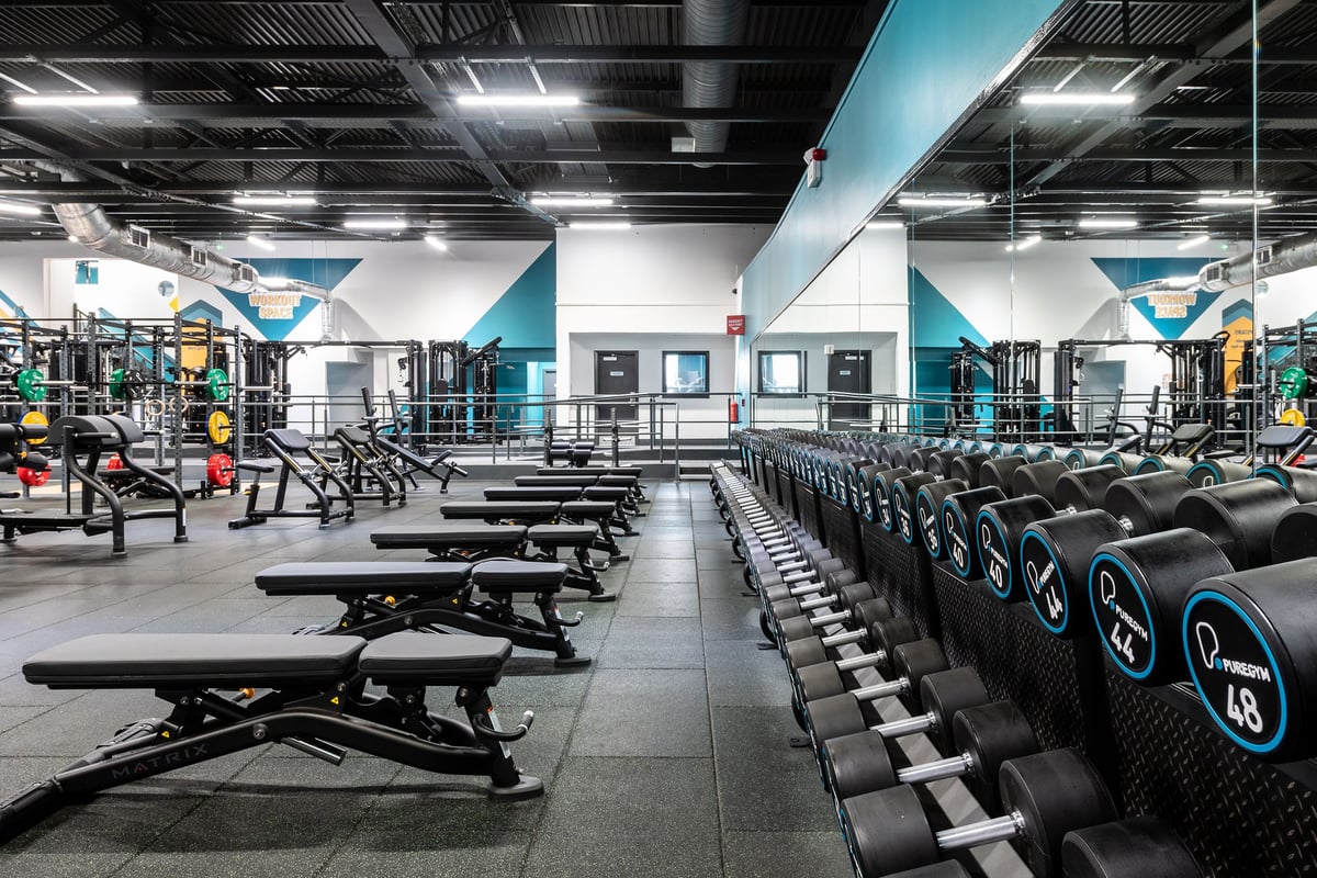 PureGym Southampton Bitterne: Rows of benches, freeweights, mirrors, and rubberized flooring in a gym with teal accents.