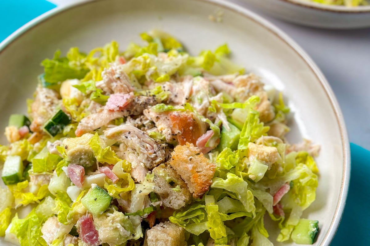 Salad with lettuce, cucumber, croutons, chicken, and diced vegetables in a bowl