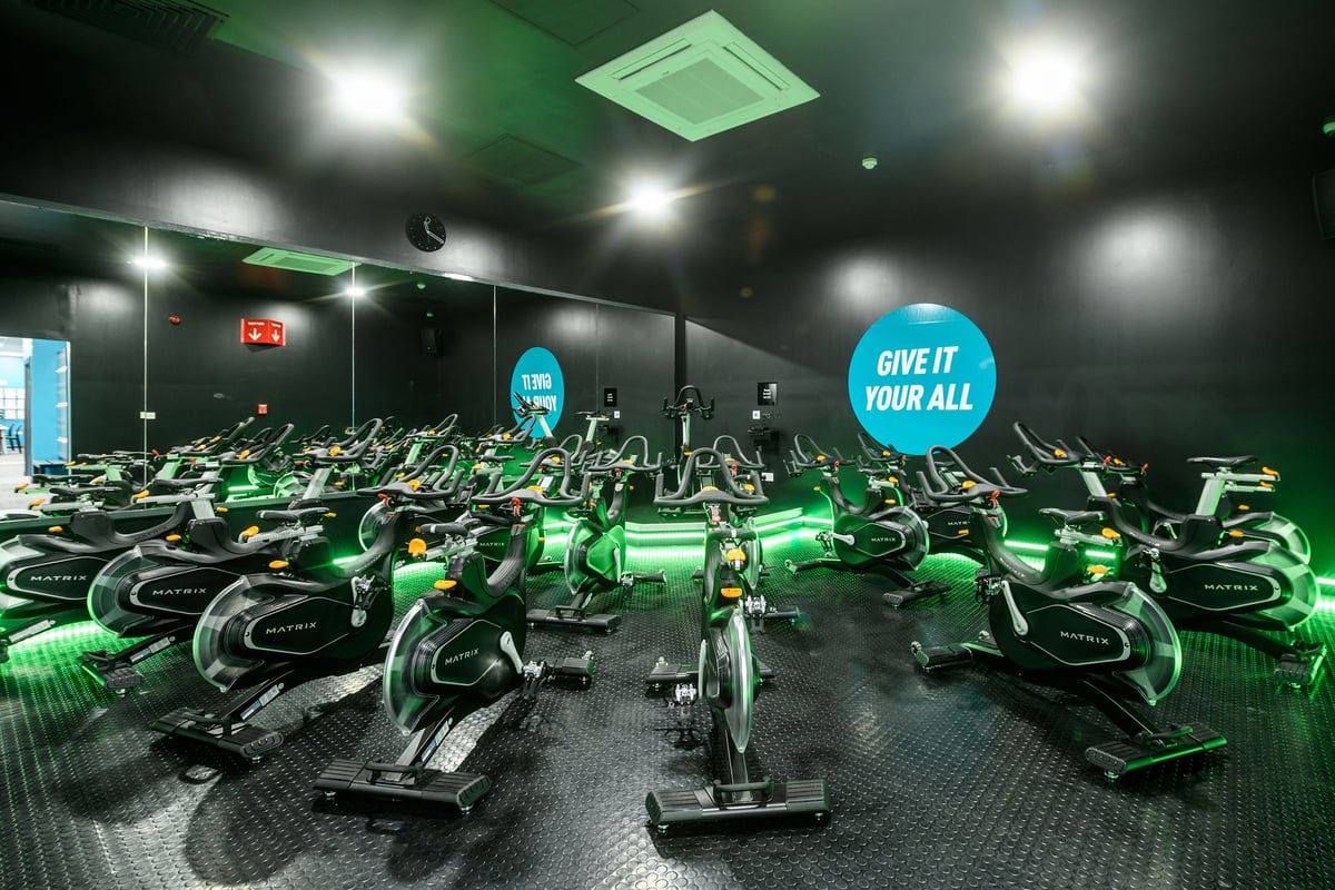 PureGym Southend Fossetts Park: Rows of stationary bikes under green neon lighting with motivational signage.