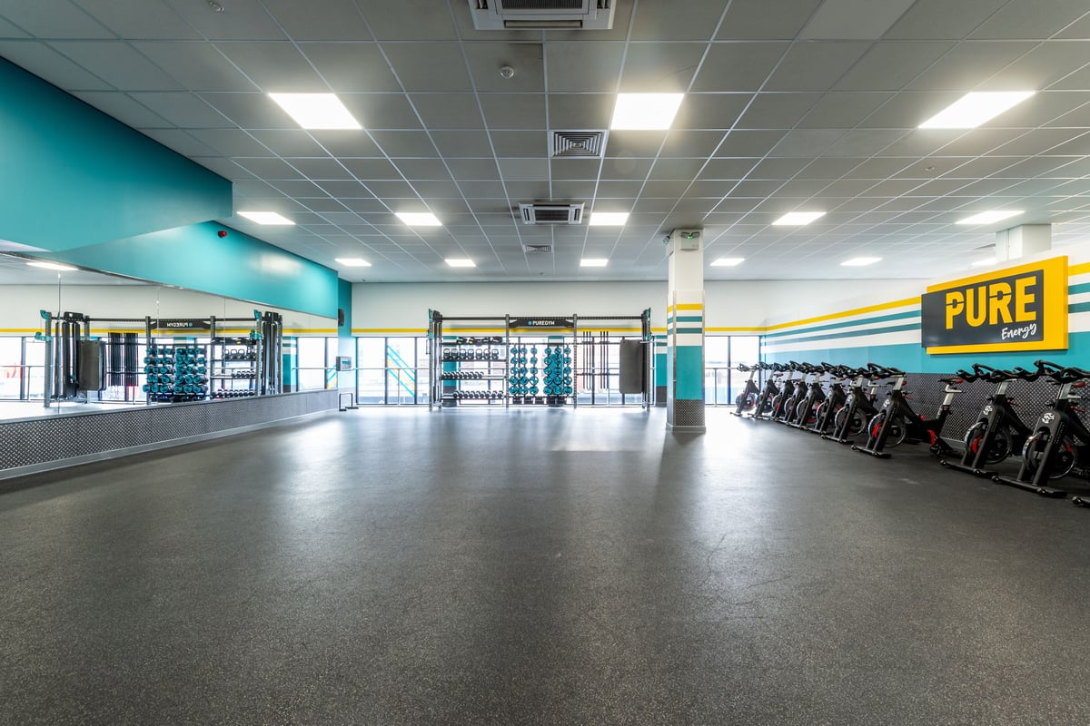 PureGym London Ilford: Rows of stationary bikes, mirrored walls, and teal accented interior space.