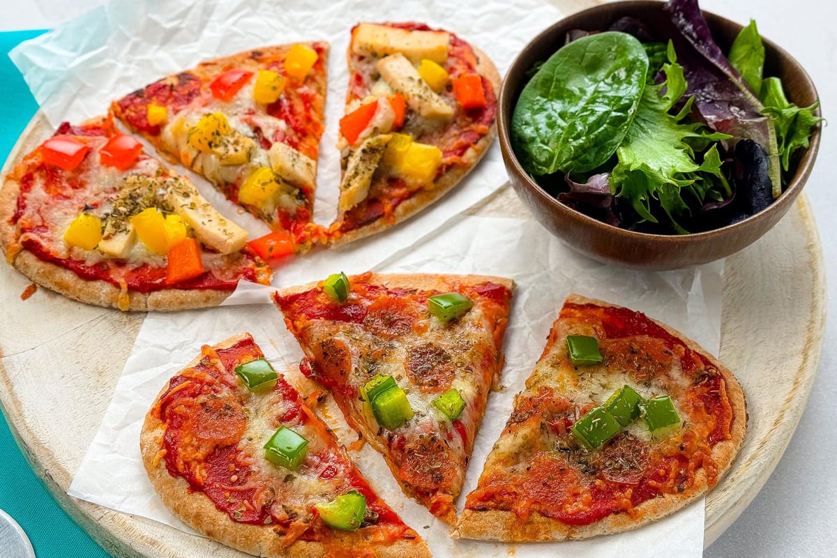 Pizza slices on wooden board with colourful toppings served with bowl of salad leaves