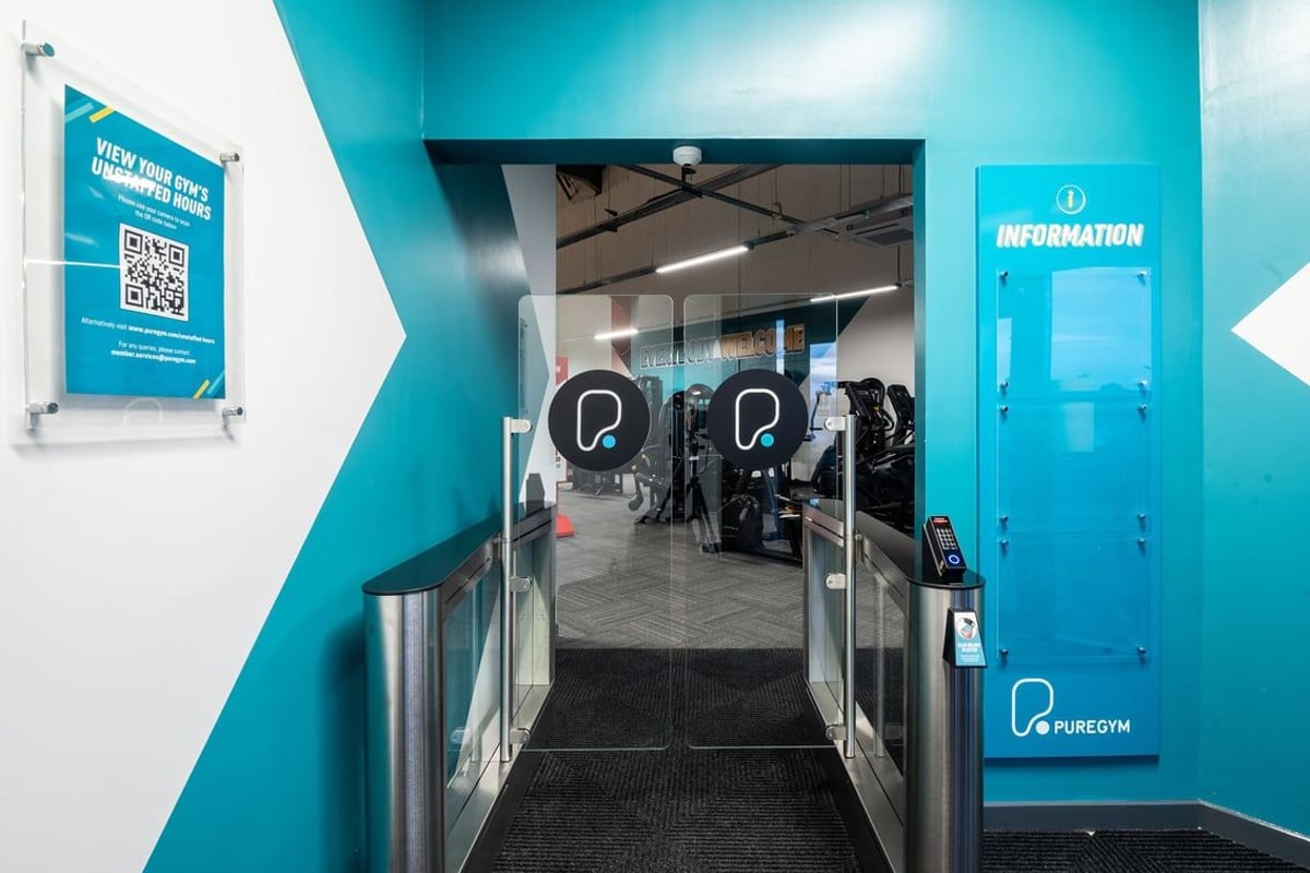 PureGym Lanark: Teal-coloured corridor with QR code poster, leading to cubicles containing exercise equipment.