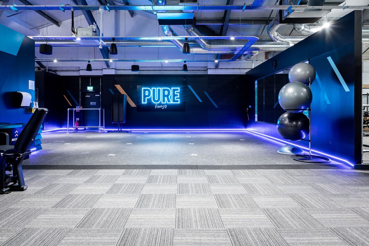 PureGym Stowmarket: Gym studio with stage area, blue lighting, and large PURE signage.