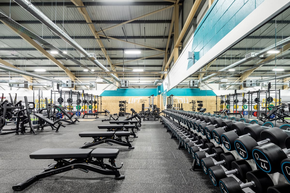 PureGym Neath: Rows of weight benches, dumbbell racks, strength training machines in a large warehouse-style gym.