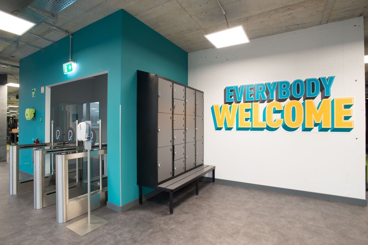 PureGym Adliswil: Entrée lumineuse de la salle de sport avec casiers et portiques d'entrée.
