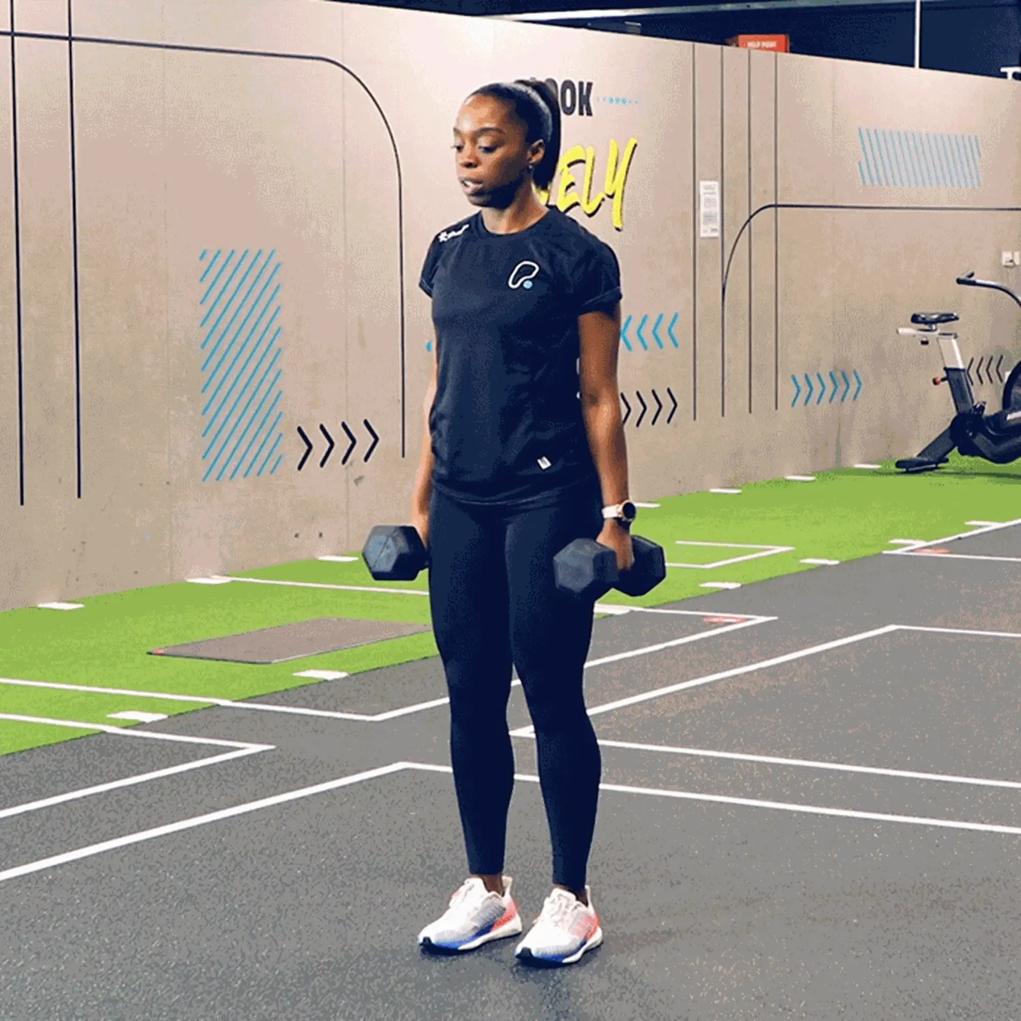 woman in black sportswear lifting dumbbells in a gym with green and grey flooring