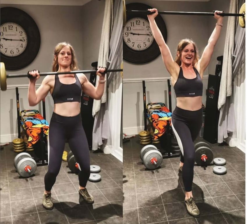 Woman lifting a barbell from shoulder height to overhead in a home gym with weights.