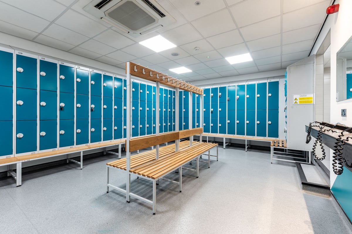 PureGym Ashton Under Lyne: Rows of blue lockers, wooden benches, and no fitness equipment visible.