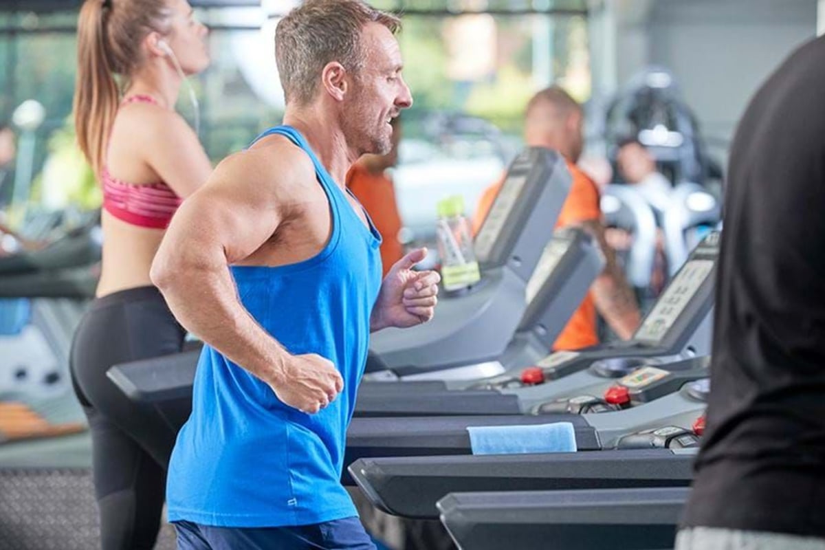 People running on treadmills in a gym with large windows in the background