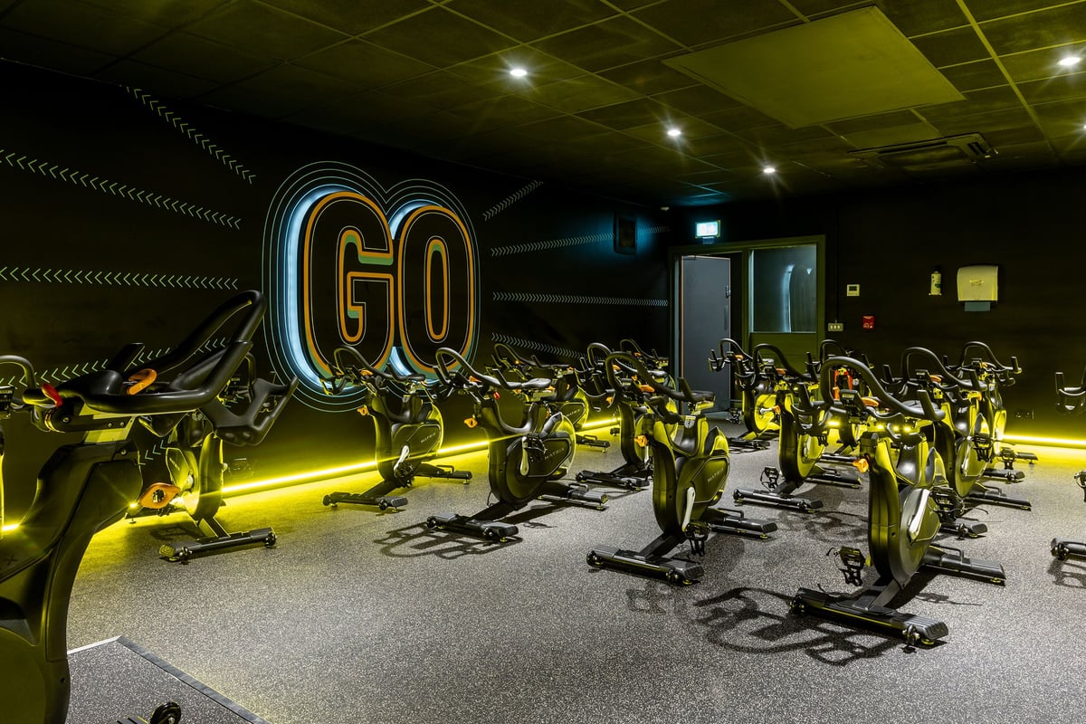 PureGym Northolt: Rows of stationary bikes on rubberised flooring, neon 'GO' signage in dimly lit studio space.