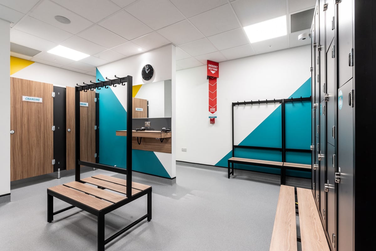 PureGym London Wood Green: Weightlifting racks, benches, mirrors along wall, colourful padded flooring.
