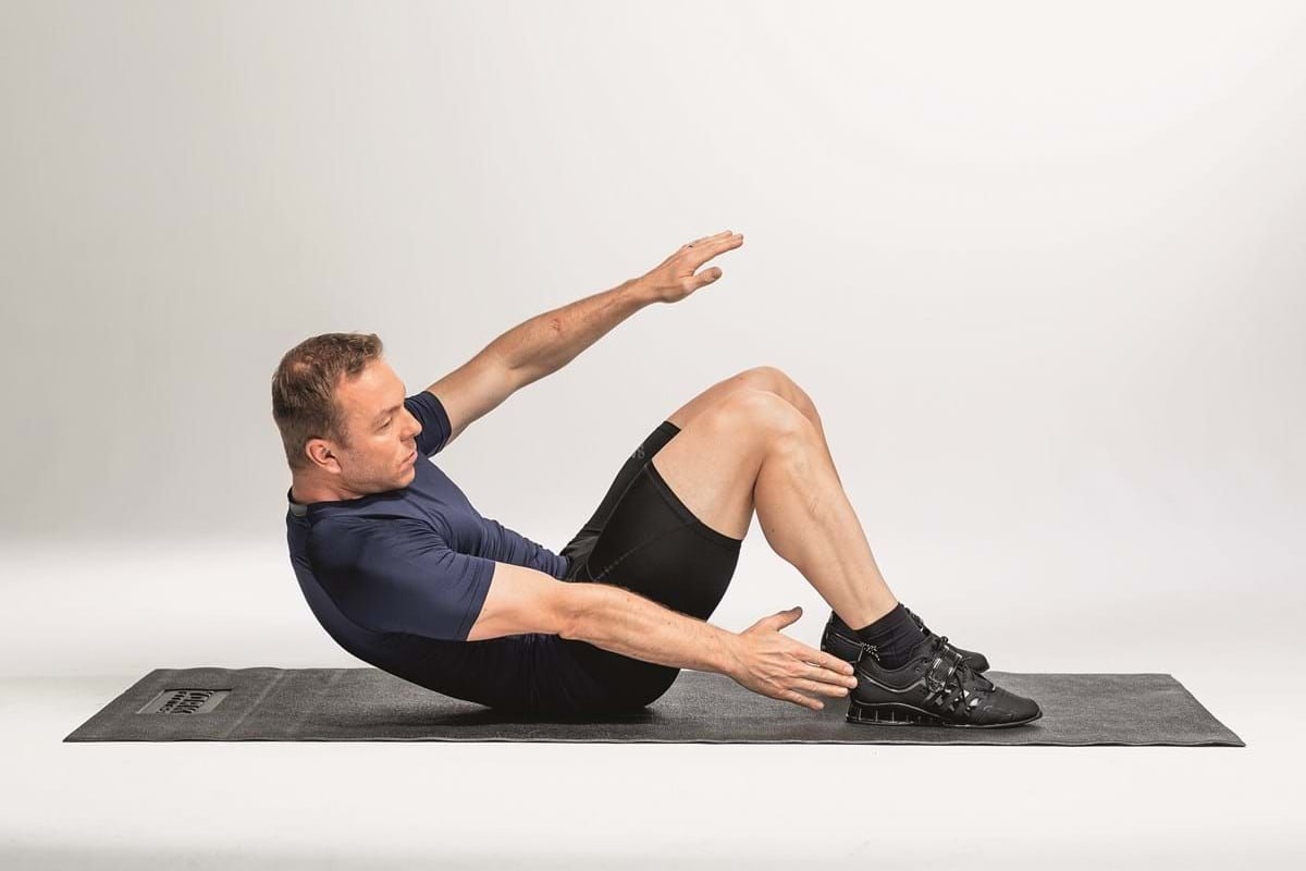Man exercising on mat doing Russian twists with bent knees and arms extended