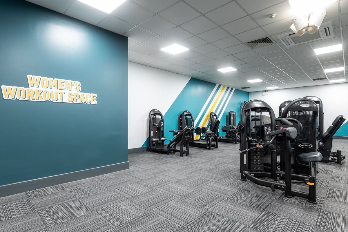PureGym Harlow: Women's workout area with resistance machine circuit stations and motivational wall graphics.
