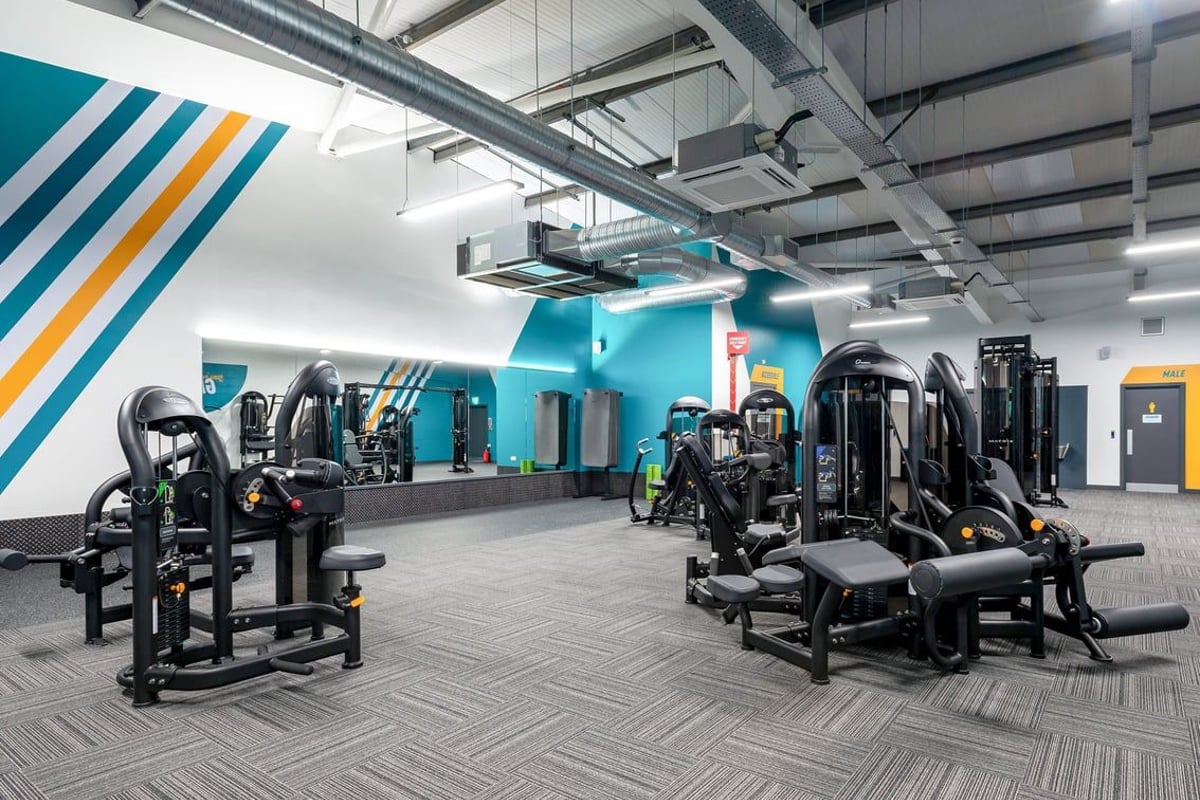 PureGym Stratford-upon-avon: Strength training equipment like chest presses, cable machines, and weight benches in a teal-accented gym space.