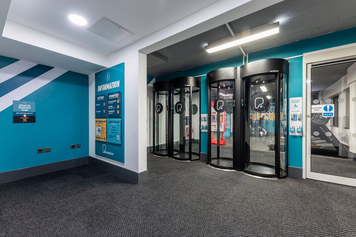PureGym London Putney: Rows of self-service kiosks, teal accents, and carpet flooring.