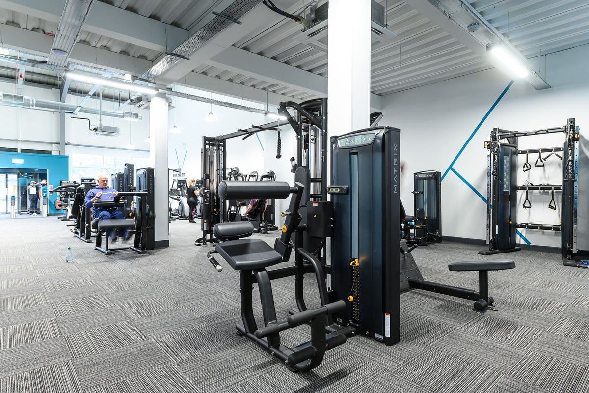 PureGym Glossop: Rows of strength training machines, benches, weight stacks, and rubberised flooring within a gym facility.