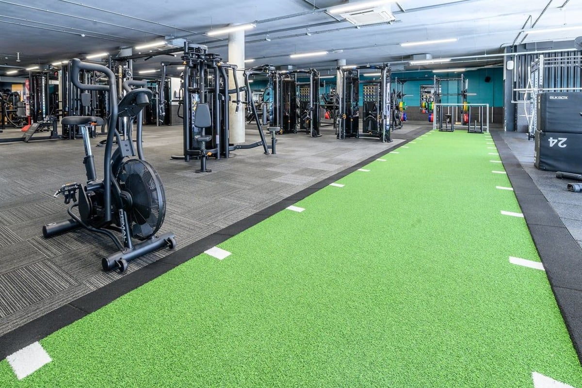 PureGym London Greenwich: Weight machines, free weights, turf area and rubberized flooring in a gym setting.