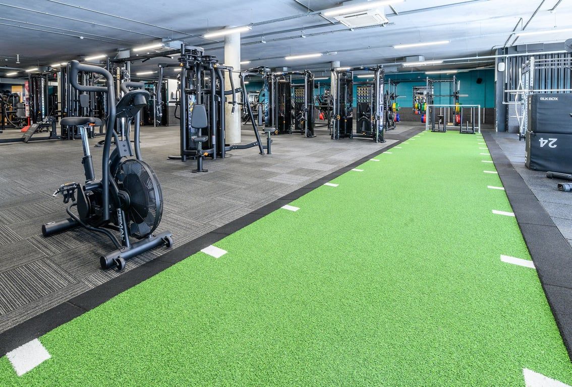 PureGym London Greenwich: Weight machines, free weights, turf area and rubberized flooring in a gym setting.