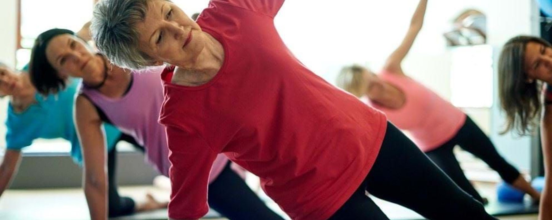 Group of women doing side plank exercise on yoga mats in a fitness studio