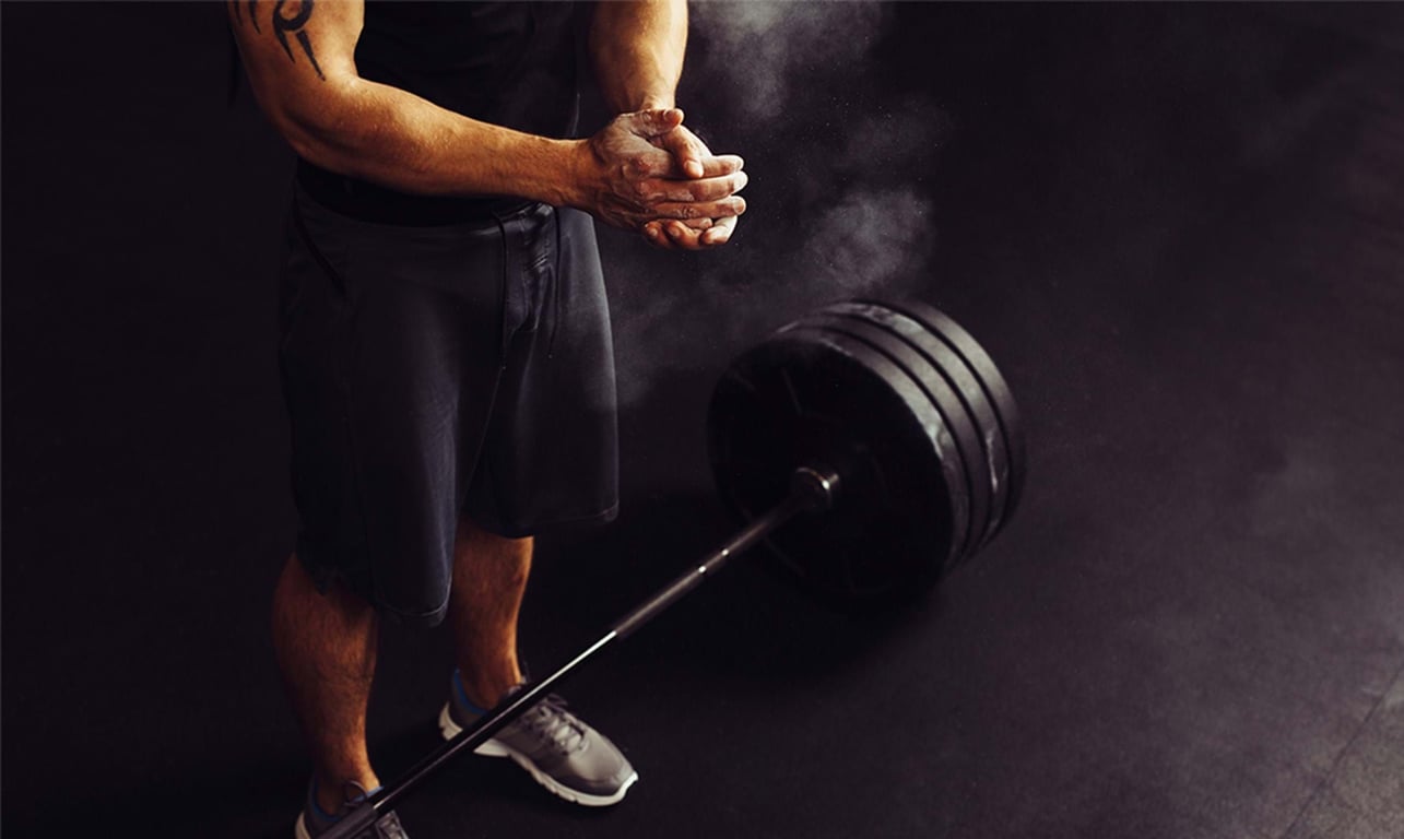 Man clapping chalked hands near a heavily weighted barbell on the floor