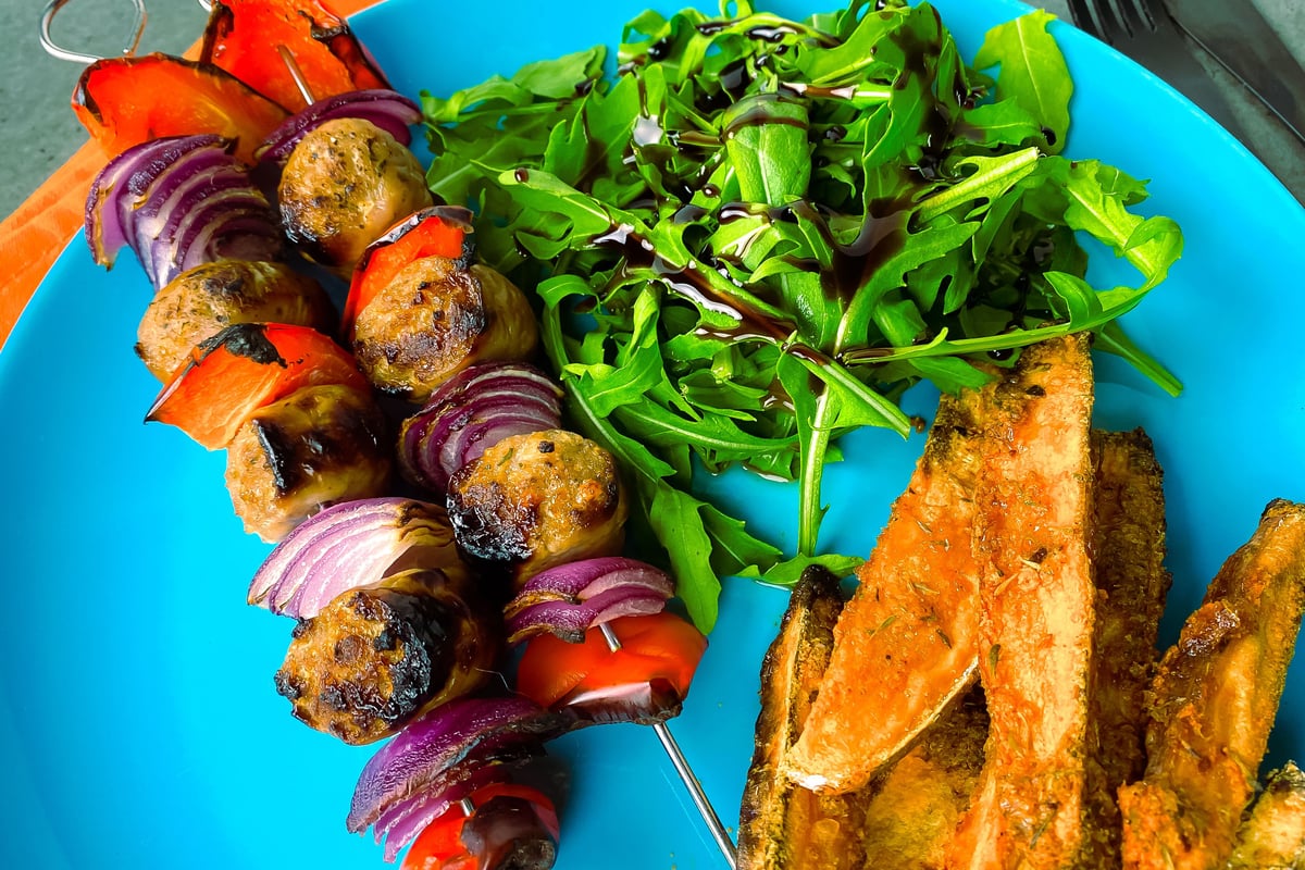 Grilled vegetable kebabs with fresh rocket salad and potato wedges on blue plate