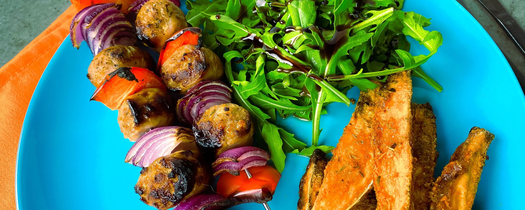 Grilled vegetable kebabs with fresh rocket salad and potato wedges on blue plate