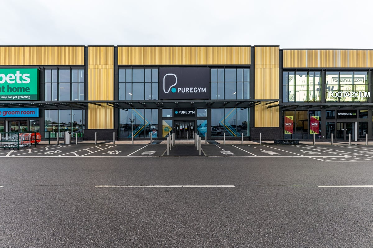 PureGym Liverpool Edge Lane: Puregym store front with parking spaces, glass facade, and wood panels.