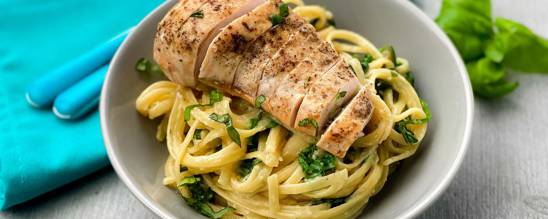 Sliced grilled chicken breast on pasta with herbs in a white bowl