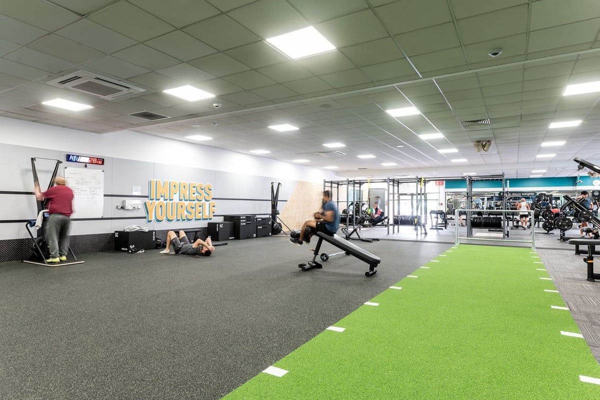 PureGym Woking: Weight racks, resistance bands, functional turf area, free weights, and motivational wall graphics.