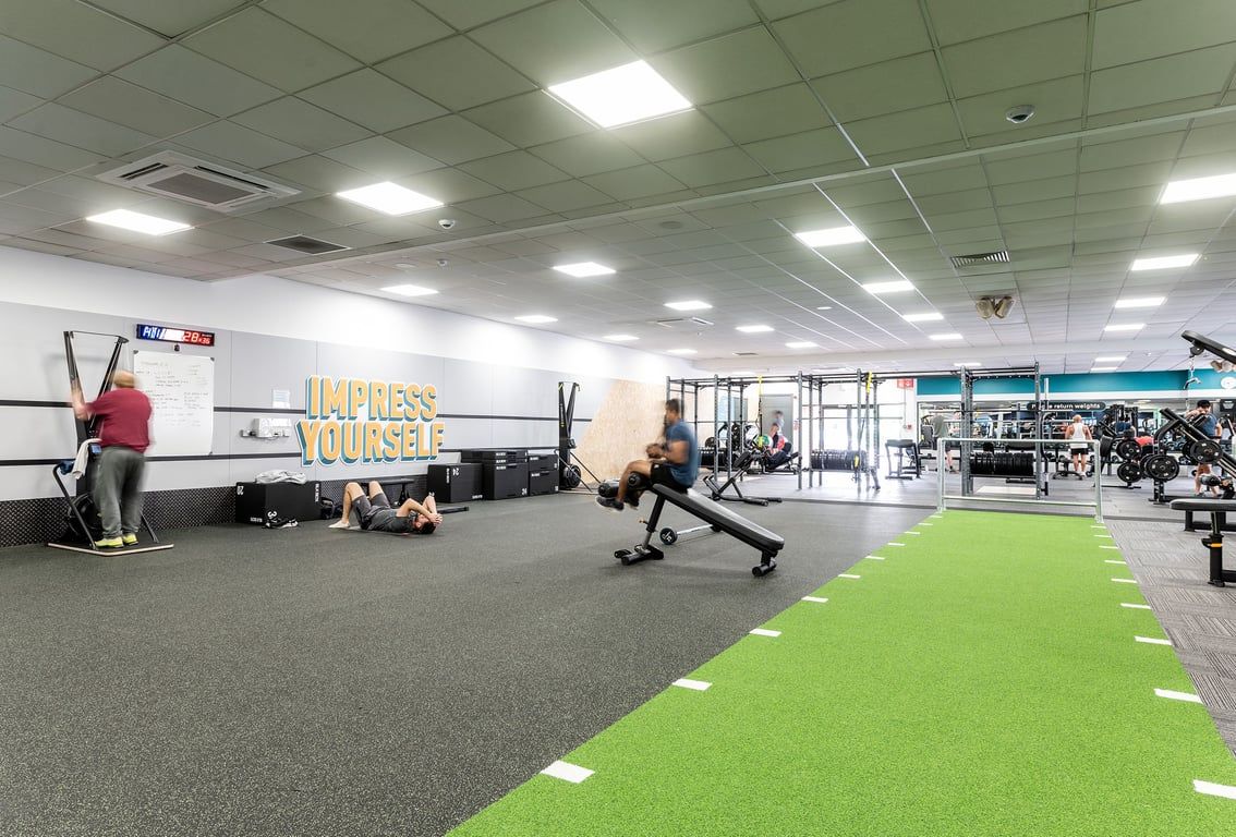PureGym Woking: Weight racks, resistance bands, functional turf area, free weights, and motivational wall graphics.