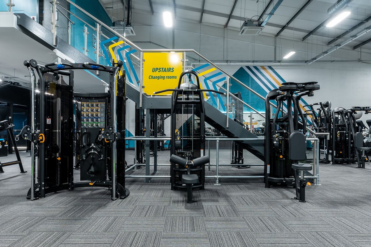 PureGym Ballymena: Weight machines, squat racks, rubberized flooring, and exercise signage in a gym facility.