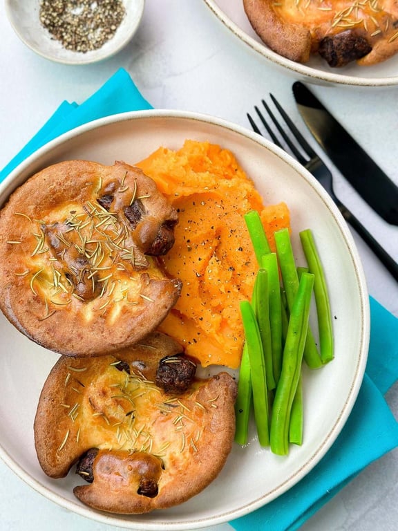 Two Yorkshire puddings with mashed sweet potatoes and green beans on a plate