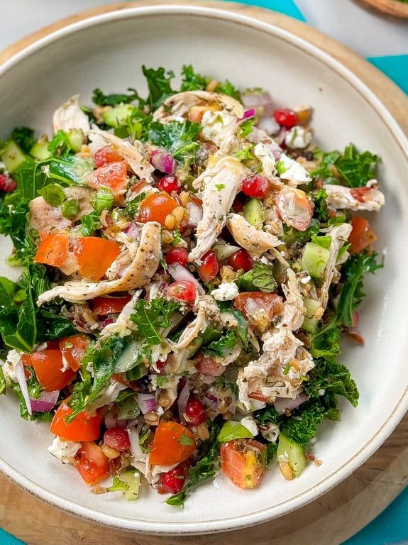 Salad with shredded chicken, kale, tomatoes, pomegranate seeds, cucumber, and onions in a