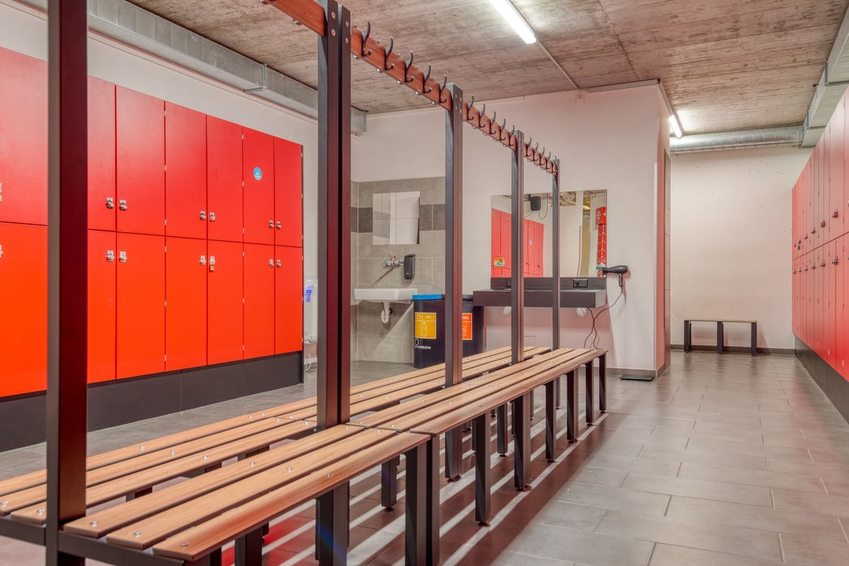 PureGym Lenzburg : vestiaires avec casiers rouges, bancs en bois et murs en miroir.