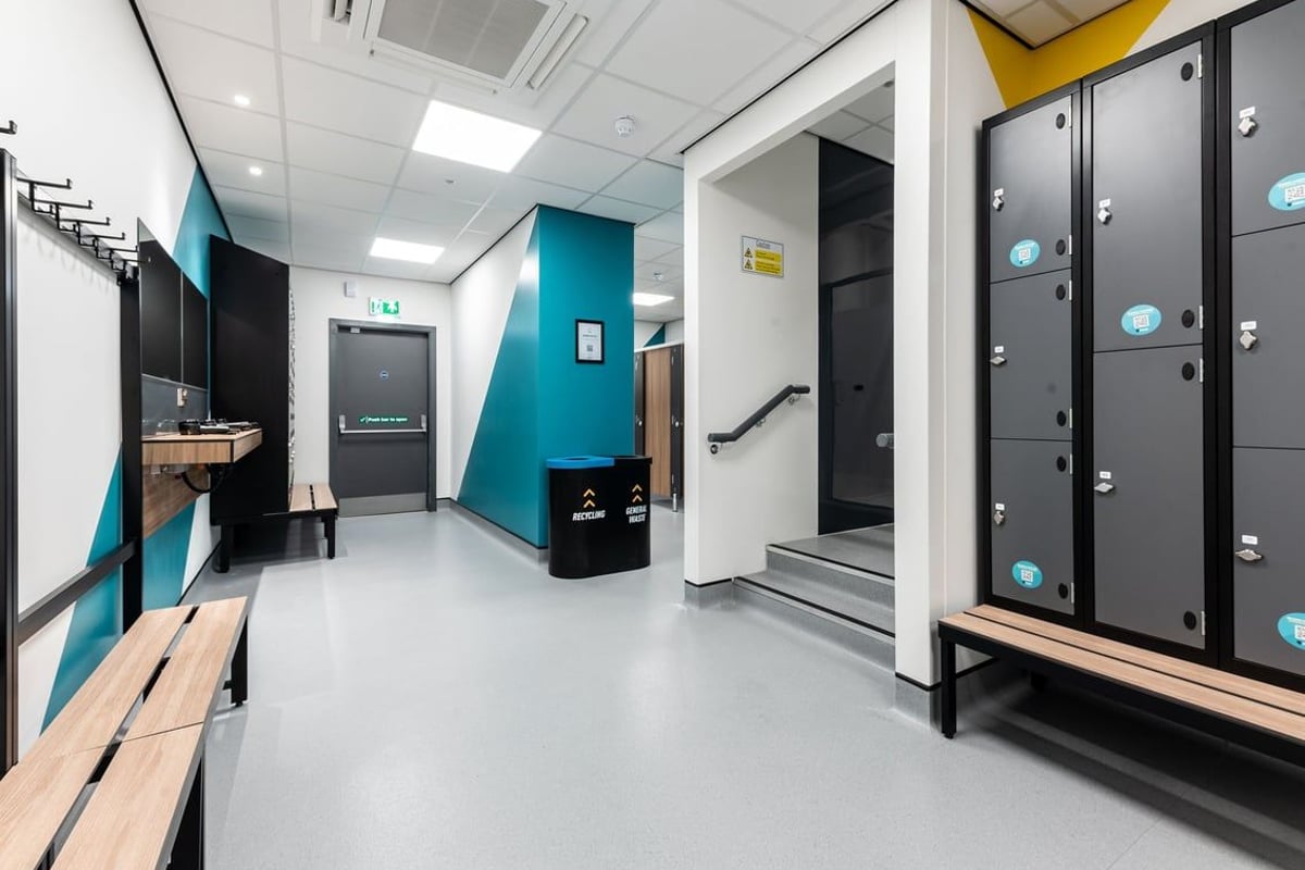 PureGym Glasgow Milngavie: Rows of lockers, benches, teal accent wall, and recycling bins.