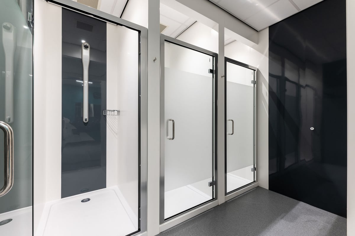 PureGym Consett: Rows of shower cubicles with glass doors, tiled walls and flooring.