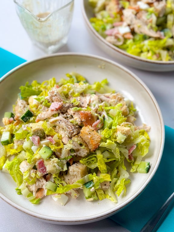 Salad with lettuce, cucumber, croutons, chicken, and diced vegetables in a bowl