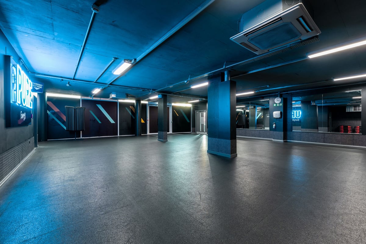 PureGym London Finsbury Park: Fitness studio with  neon blue lighting, mirrors, and rubberised flooring.