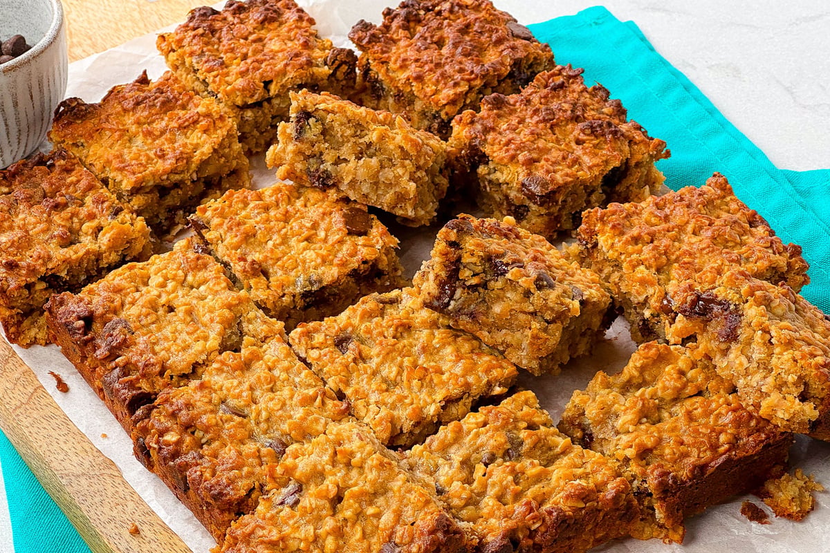 Golden oat bars with chocolate chips arranged on parchment paper with turquoise cloth